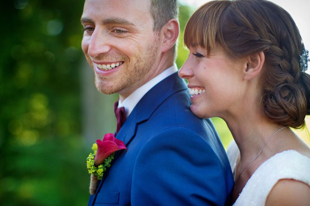 A couple shares a candid moment outdoors in formal wedding attire with natural greenery.