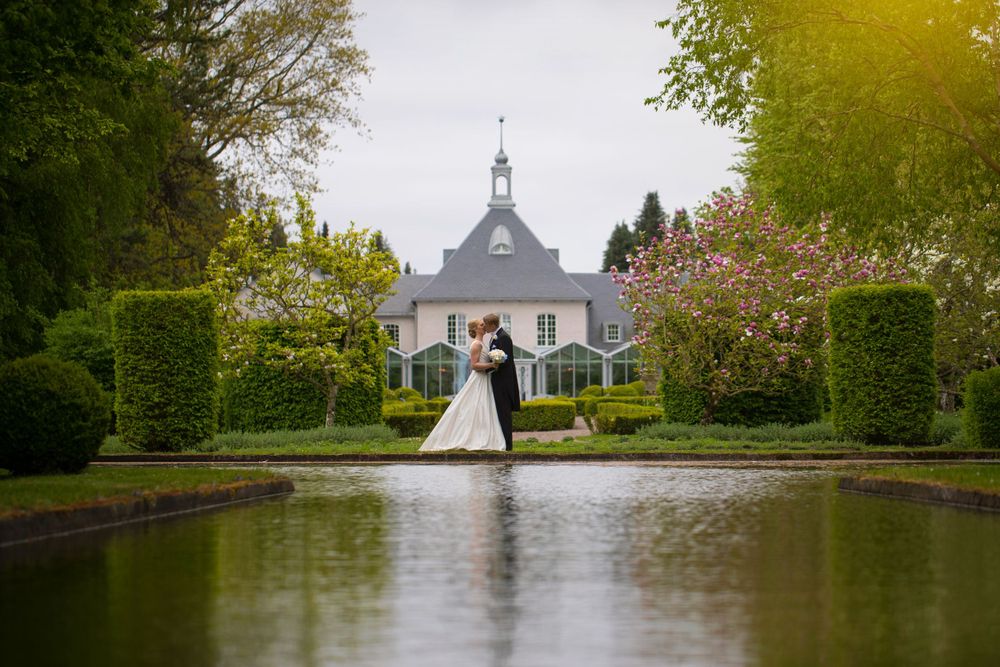 Wedding couple silhouetted in front of elegant mansion with reflecting pool.