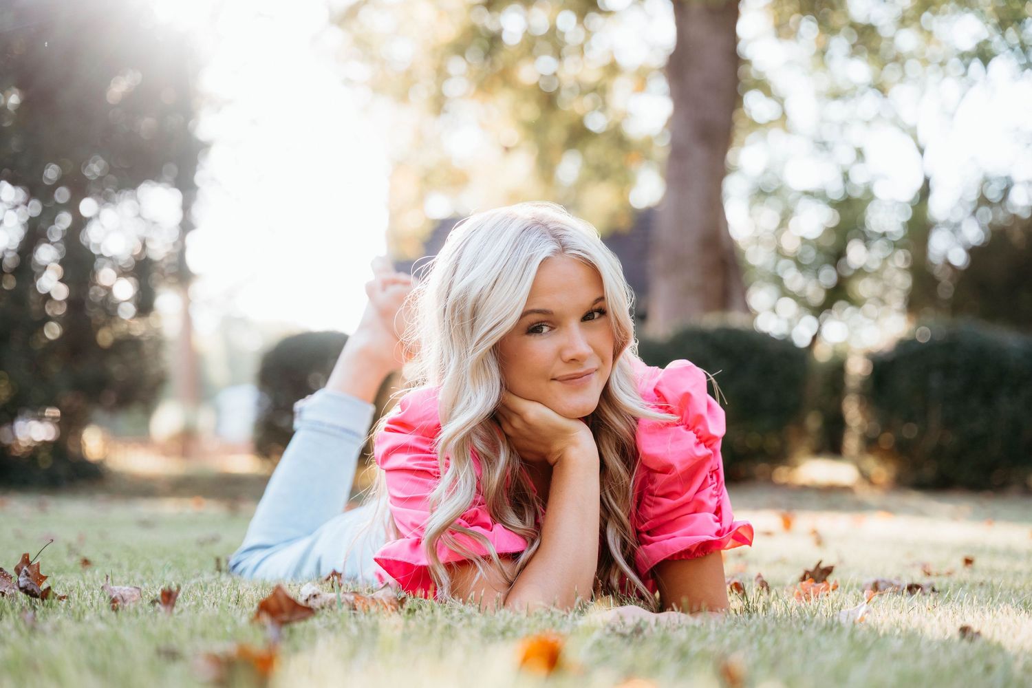 Person in white lying in autumn leaves during golden hour photography session.