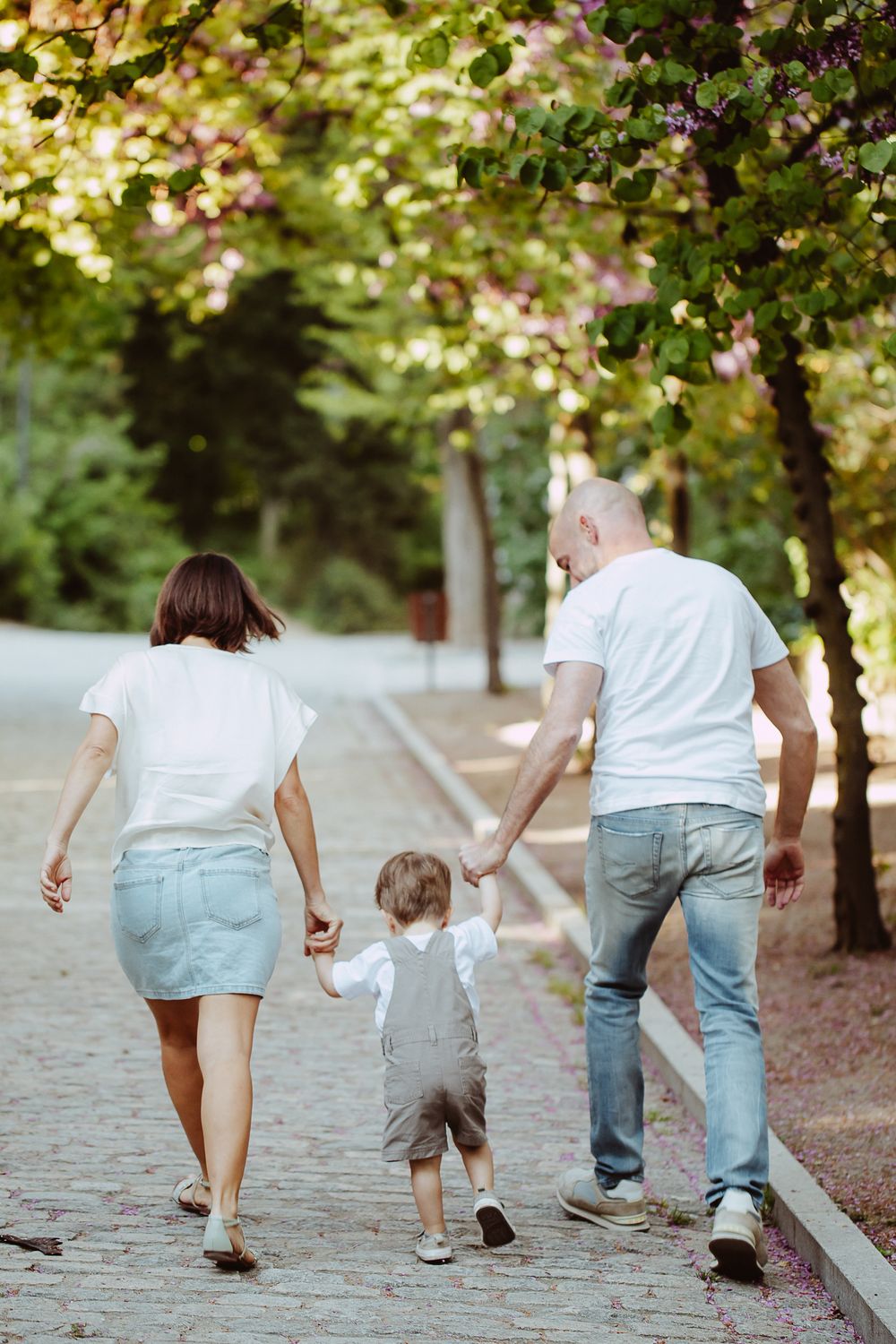 Family walking together on a tree-lined cobblestone path in casual attire.
