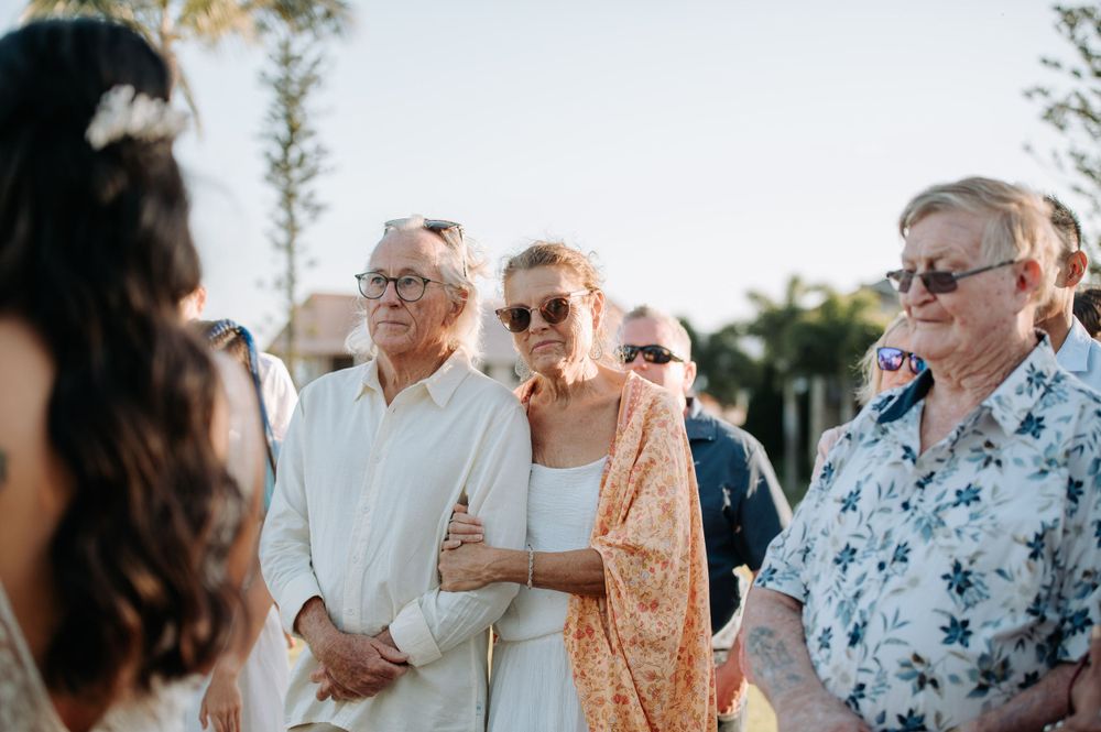 A small group of wedding guests watch with emotion during an outdoor ceremony.