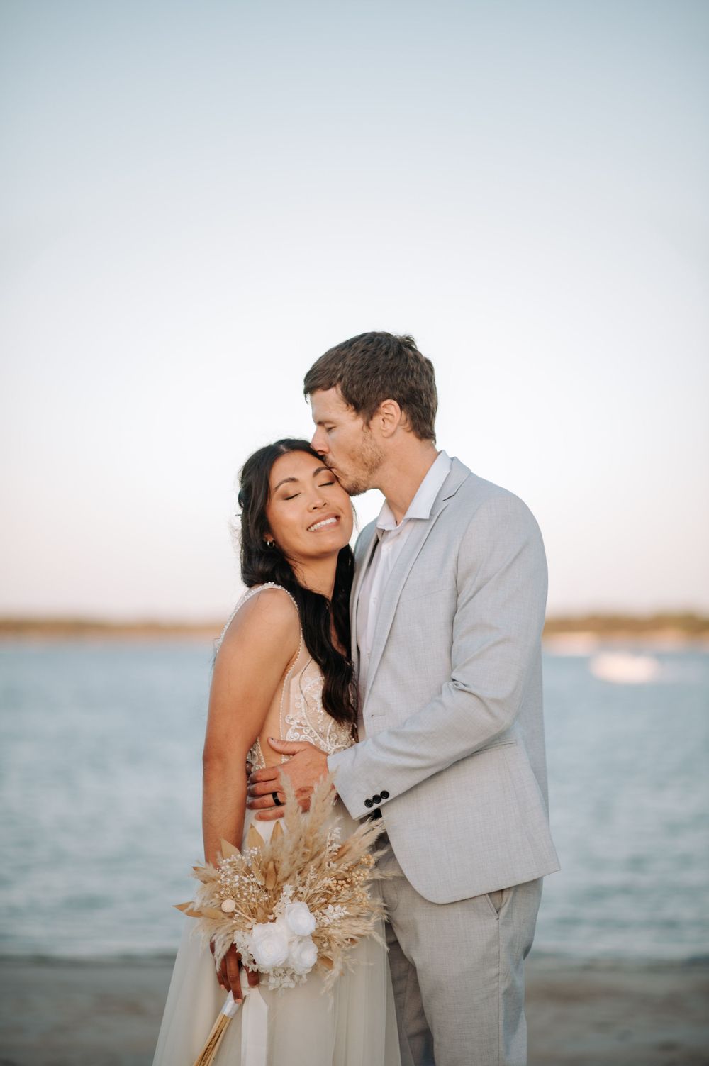 Intimate beach wedding portrait with couple embracing at sunset.
