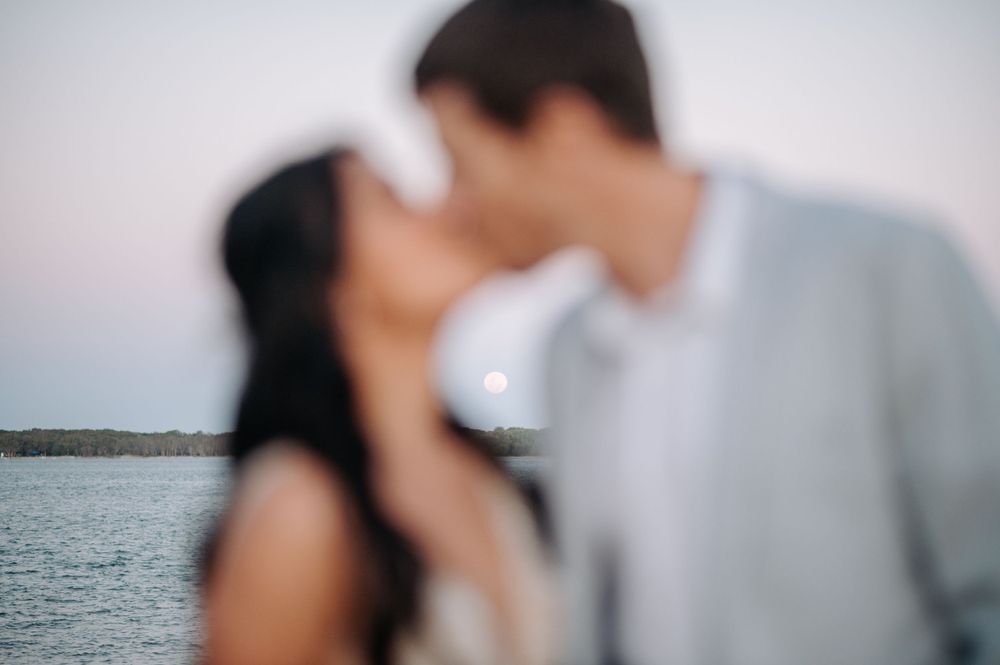An intimate romantic moment captured in soft focus against a waterfront backdrop.
