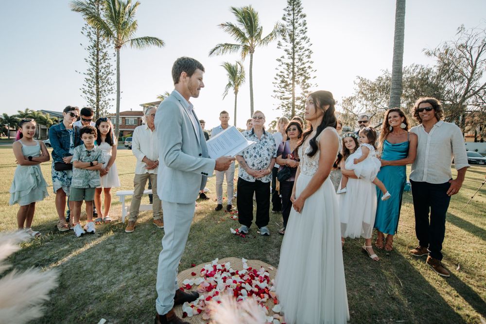 An outdoor wedding ceremony with guests gathered around in a tropical beach setting with palm trees.