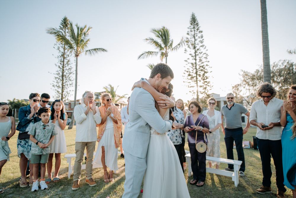 A romantic wedding ceremony under palm trees with guests applauding.