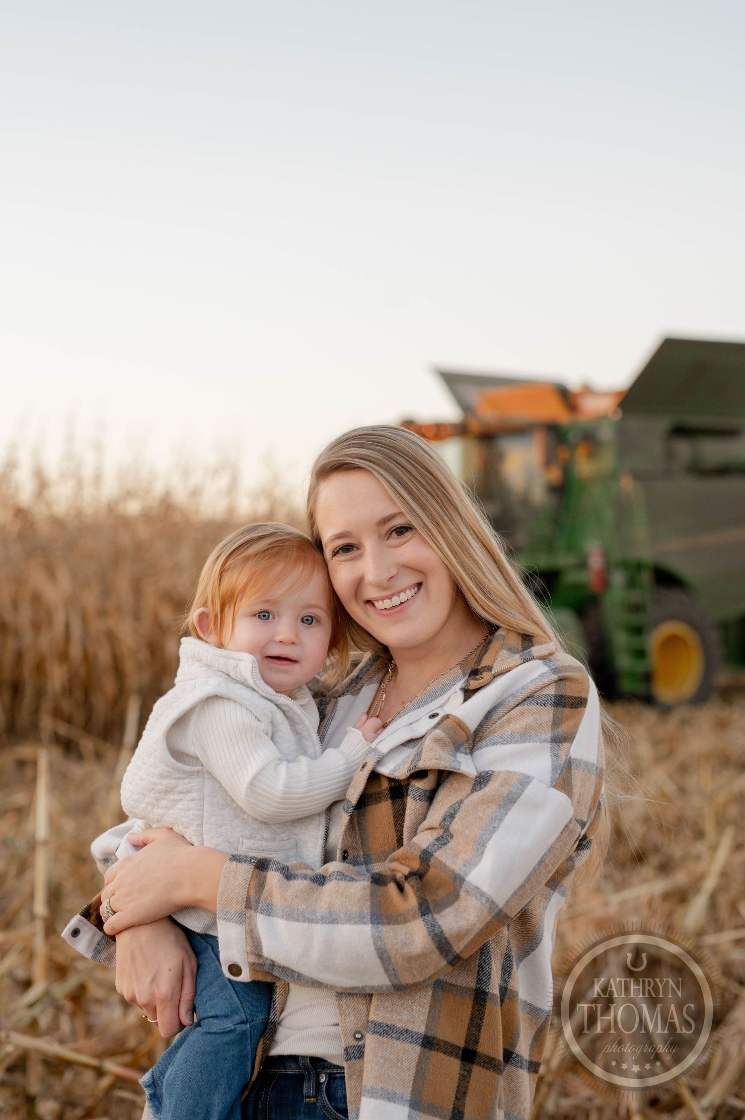 Mother and child pose in front of John Deere combine during harvest season.