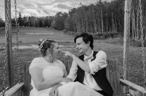 A couple sharing a playful moment while sitting together on a wooden swing in a scenic outdoor setting.