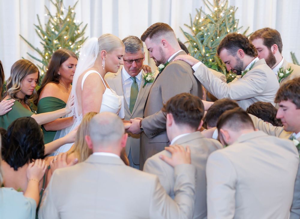A wedding party gathers in a circle for an intimate prayer moment during the ceremony.