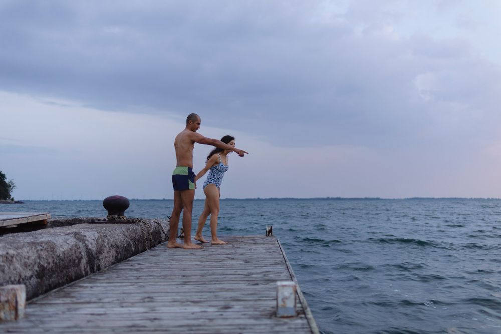 A couple holds hands as they run to jump off a dock into Lake Ontario, in Kingston, Ontario, Canada. He points at something in the water.