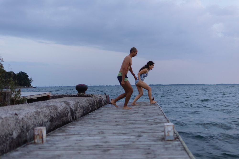A couple runs/jumps in the air from a dock into Lake Ontario, in Kingston, Ontario, Canada. They are mid stride.