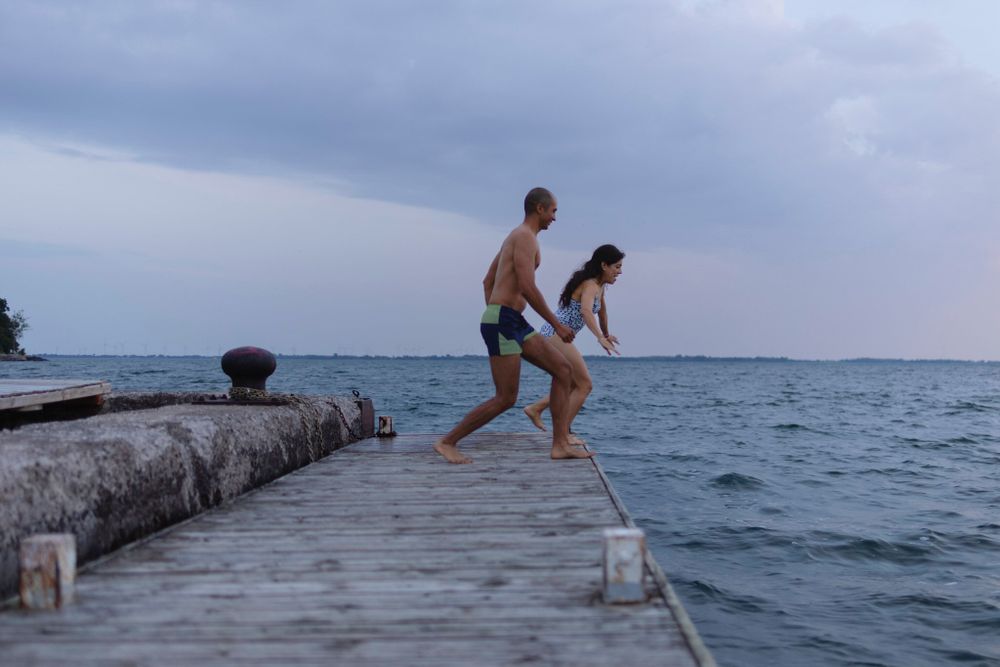 A couple runs/jumps in the air from a dock into Lake Ontario, in Kingston, Ontario, Canada. They are mid stride.