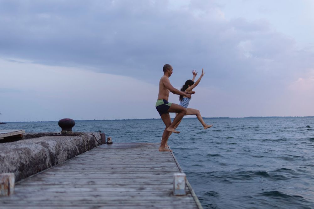 A couple runs/jumps in the air from a dock into Lake Ontario, in Kingston, Ontario, Canada. Their arms and legs are spread wide in the air.