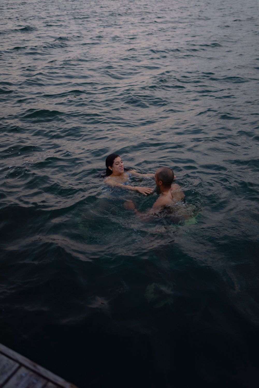 A couple swims in dark waters of Lake Ontario in Kingston, Ontario, Canada. They laugh and smile as they wade in the water.