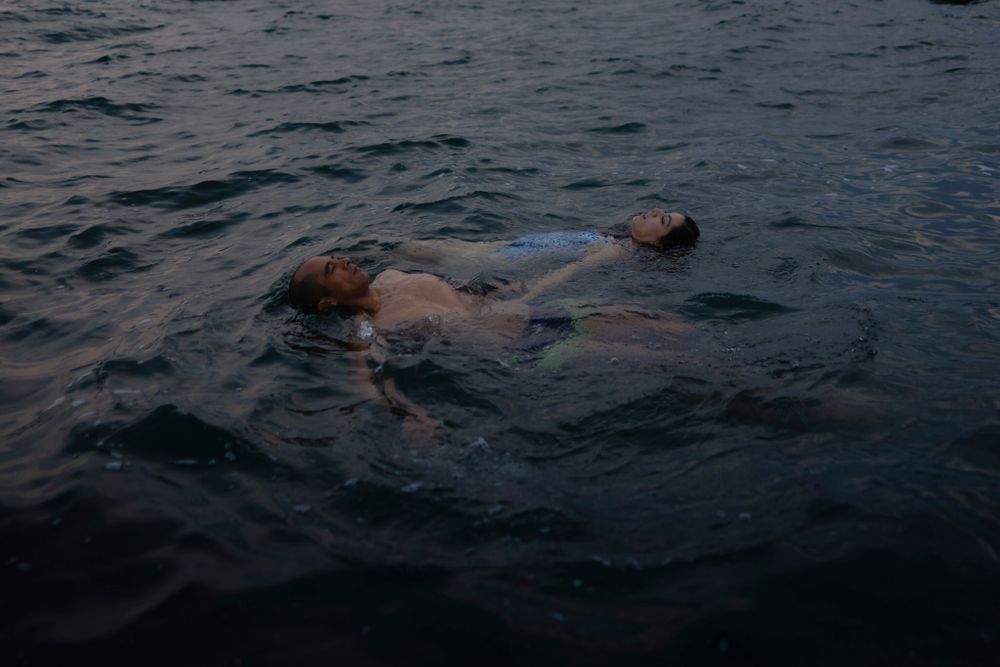 A couple swims in Lake Ontario, Kingston, Ontario, Canada. They float on their backs in opposite directions, holding hands.