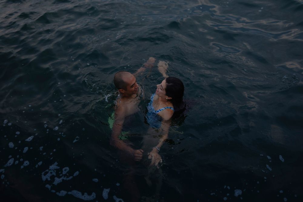 A couple swims in dark waters of Lake Ontario in Kingston, Ontario, Canada. They laugh and smile as they wade in the water.