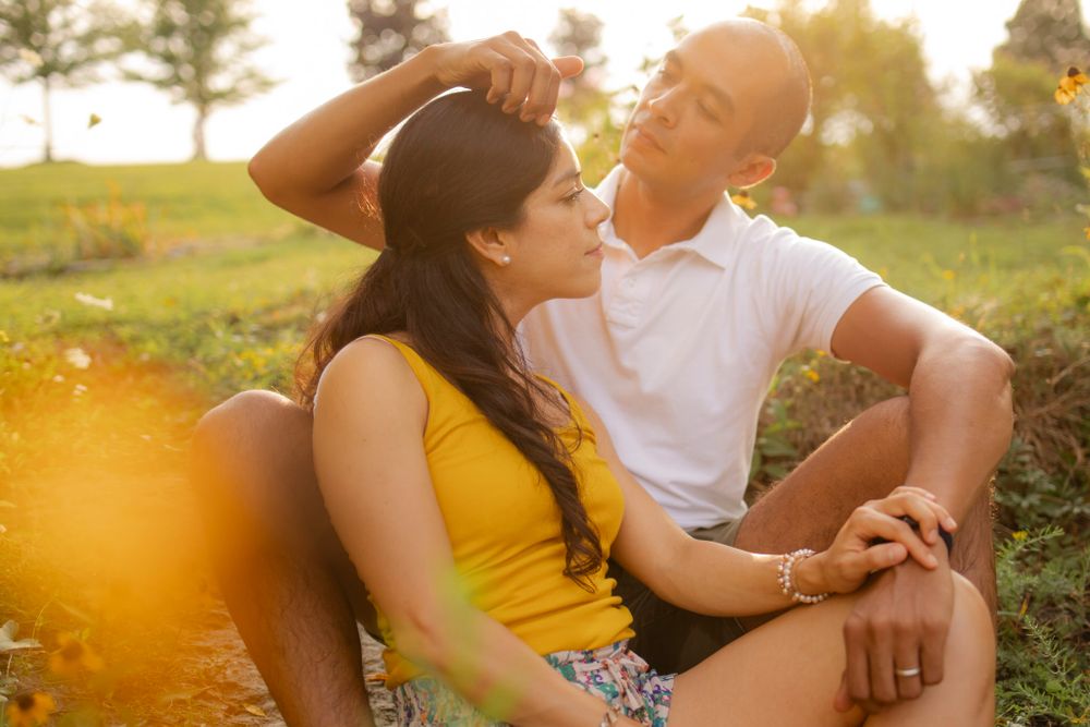 Couple sits among yellow flowers at sunset/golden hour. He reaches to fix her hair. Kingston, ON, CA.
