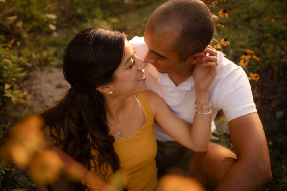 Couple sits among yellow flowers at sunset/golden hour. Tight shot of them sitting nose to nose at Lake Ontario, Kingston, ON, CA.