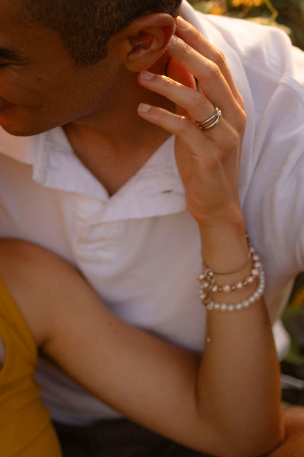 Couple sits among yellow flowers at sunset/golden hour. Tight shot her hand on his neck at Lake Ontario, Kingston, ON, CA.