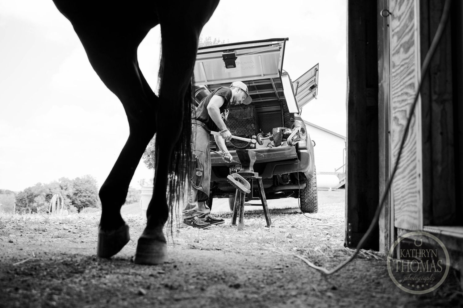 Black and white image of a horse's silhouette near a vintage car being loaded.