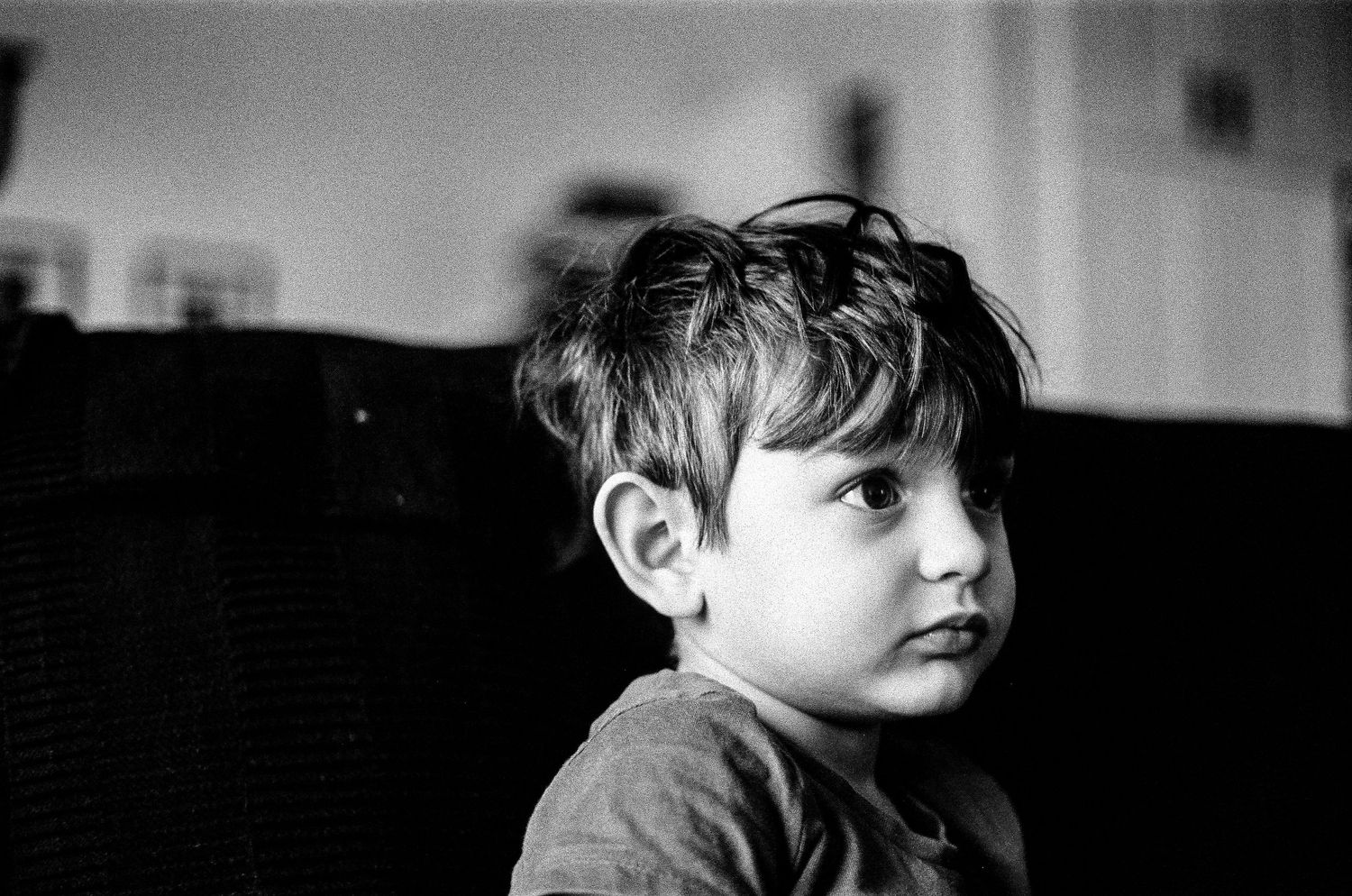 Black and white portrait photograph of a young child with tousled dark hair looking contemplatively to the side.