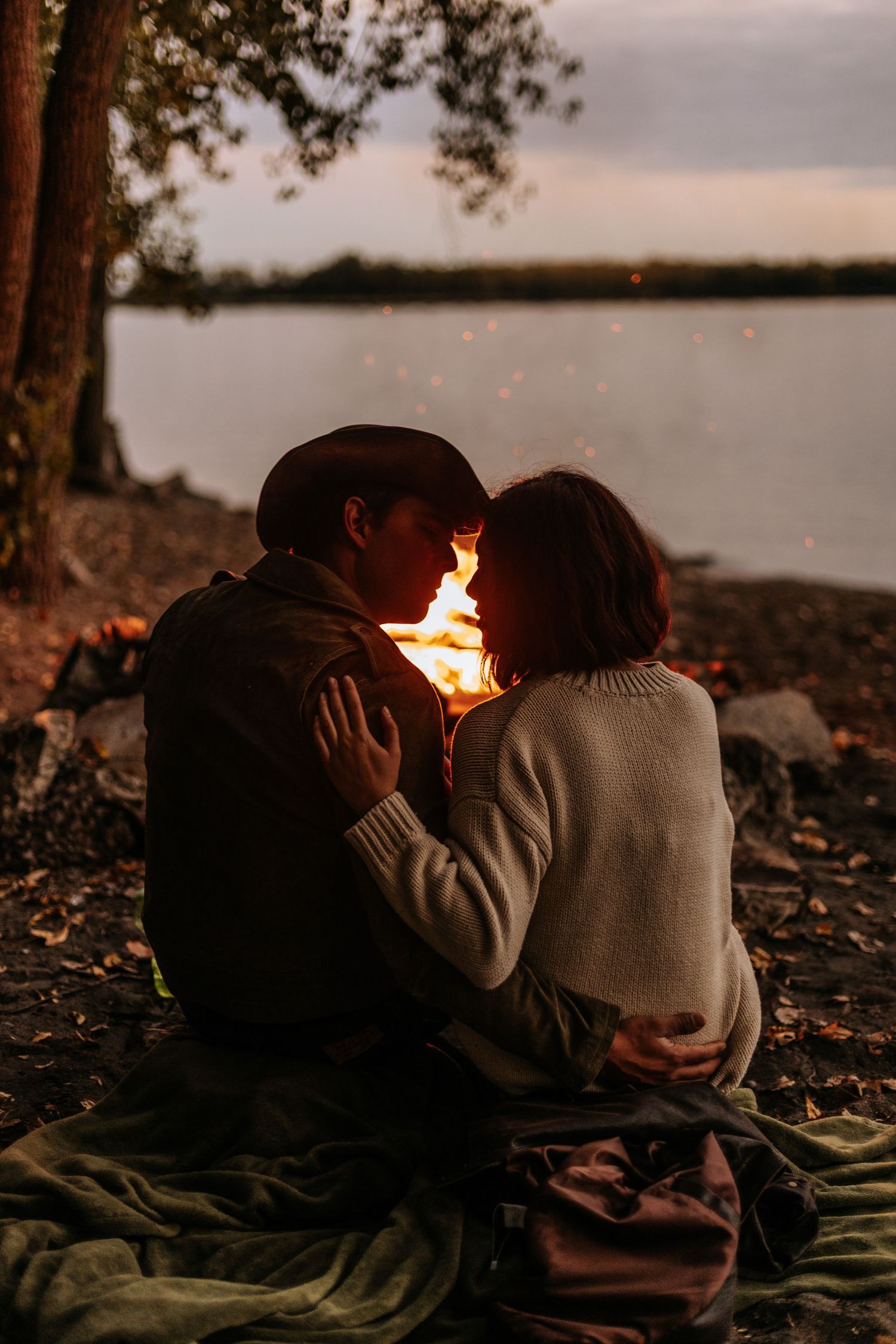 couple sitting on the lakeshore, behind of a bonfire looking at each other