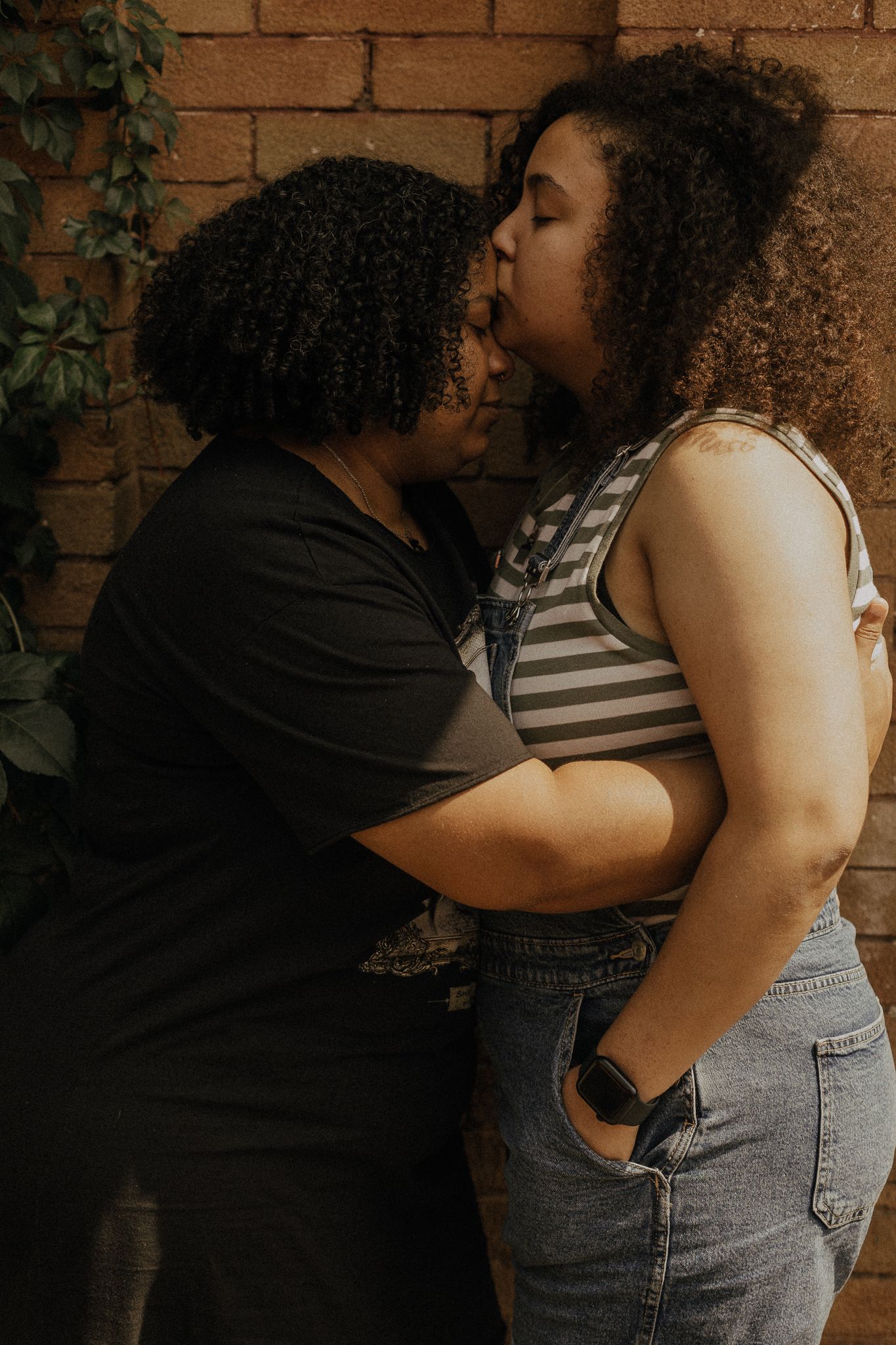 a girls couple posing for a photo, with one giving a kiss in the other one's forehead, in Toronto.