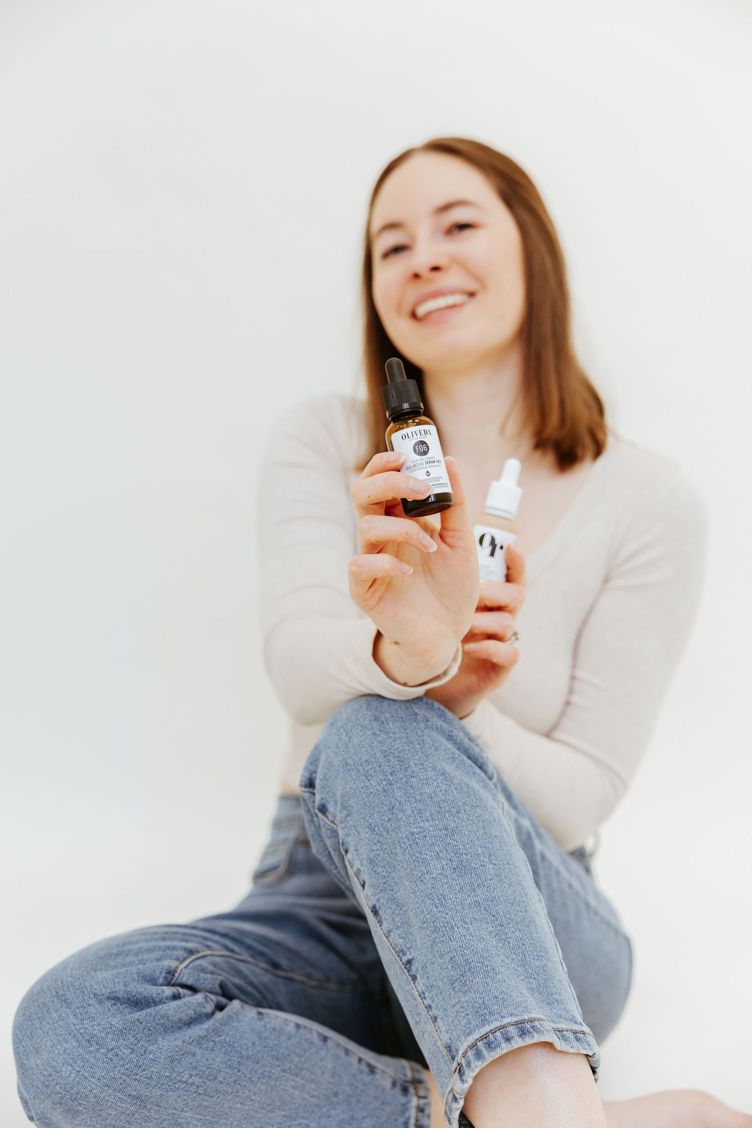 Person in cream sweater showing CBD oil products against white backdrop.