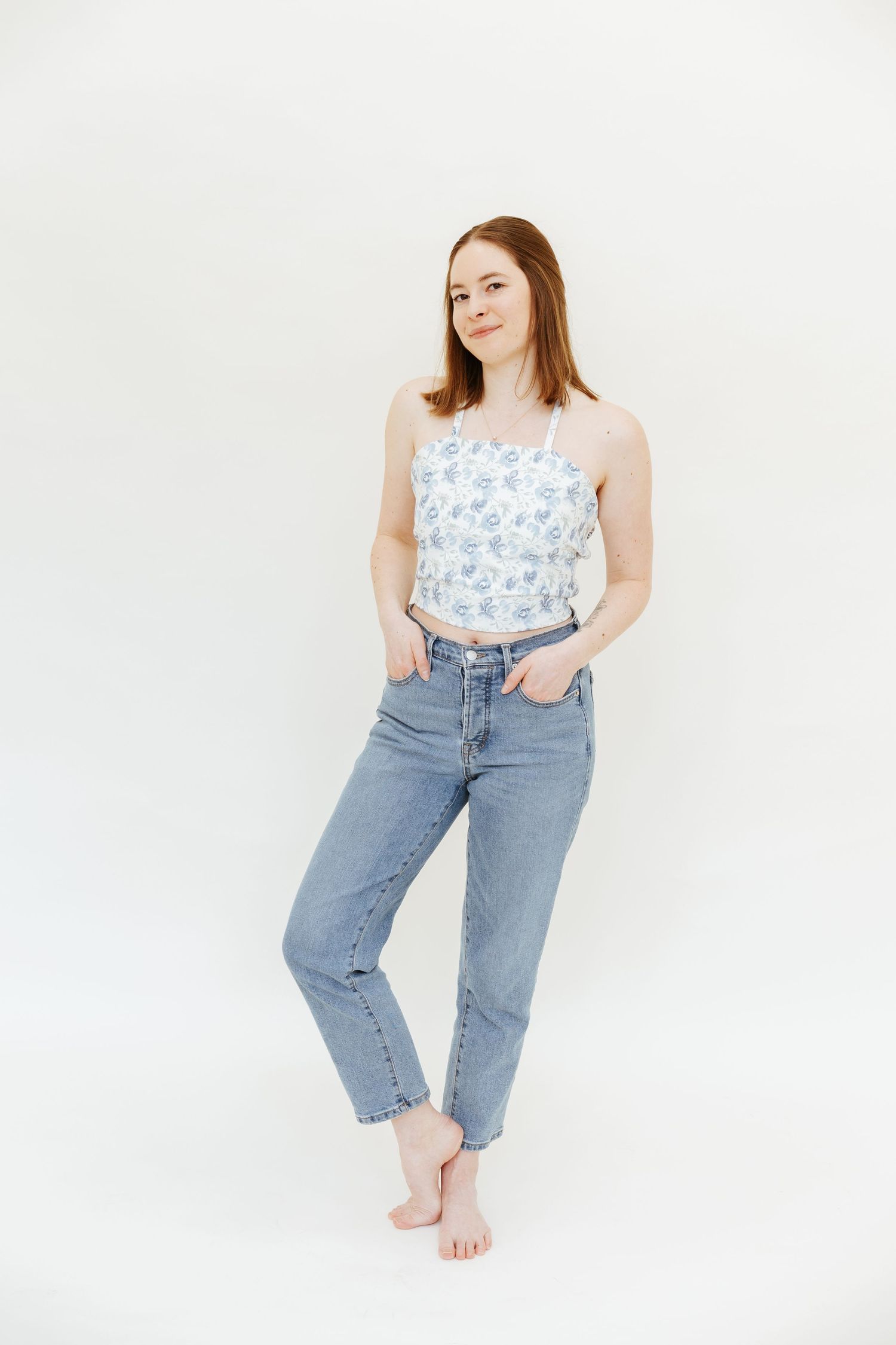 Woman in casual denim and floral top poses confidently against white backdrop.