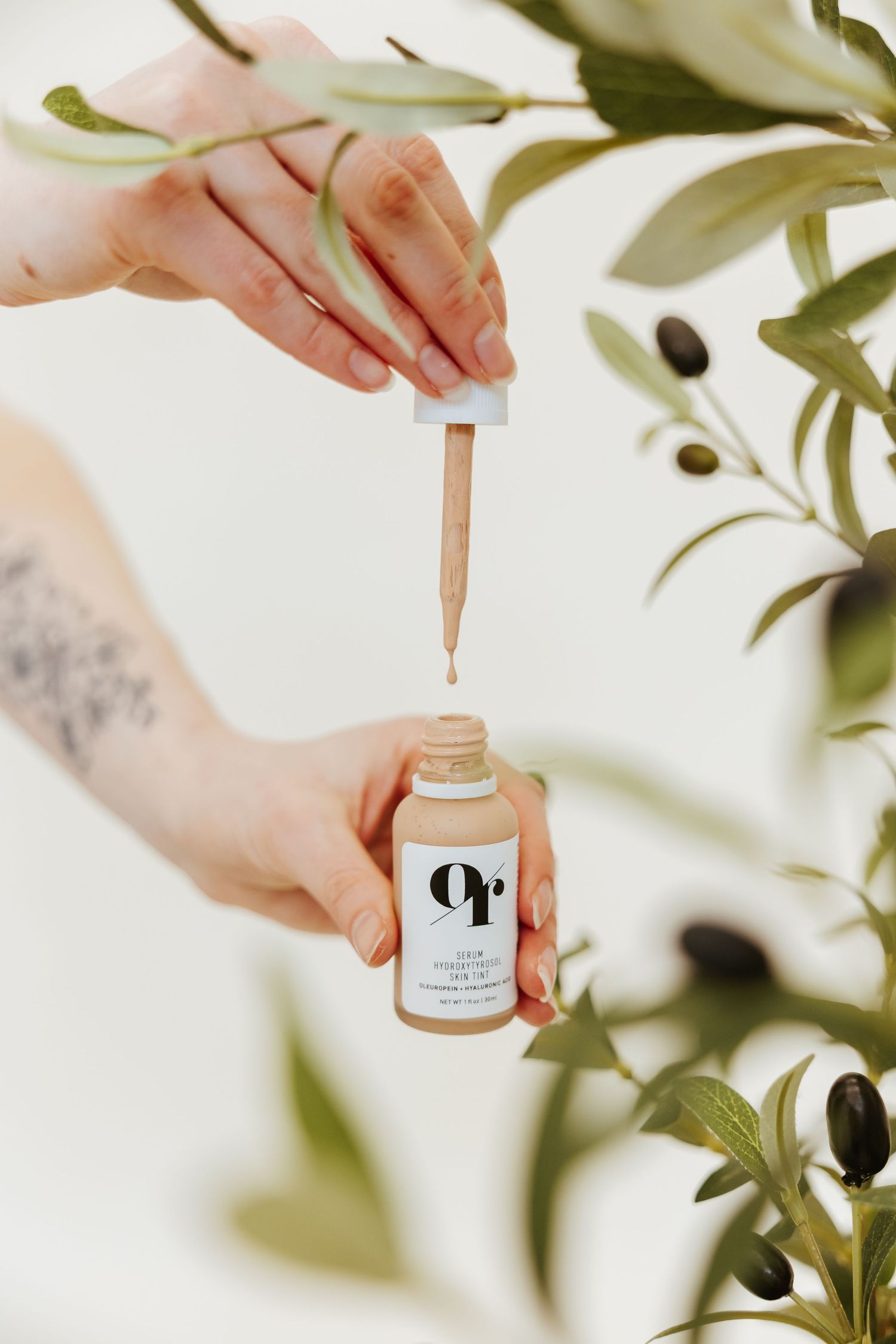 Hands holding dropper bottle with decorative plant leaves in soft lighting.