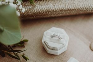 A diamond engagement ring sits in an octagonal white ring box on a textured surface.