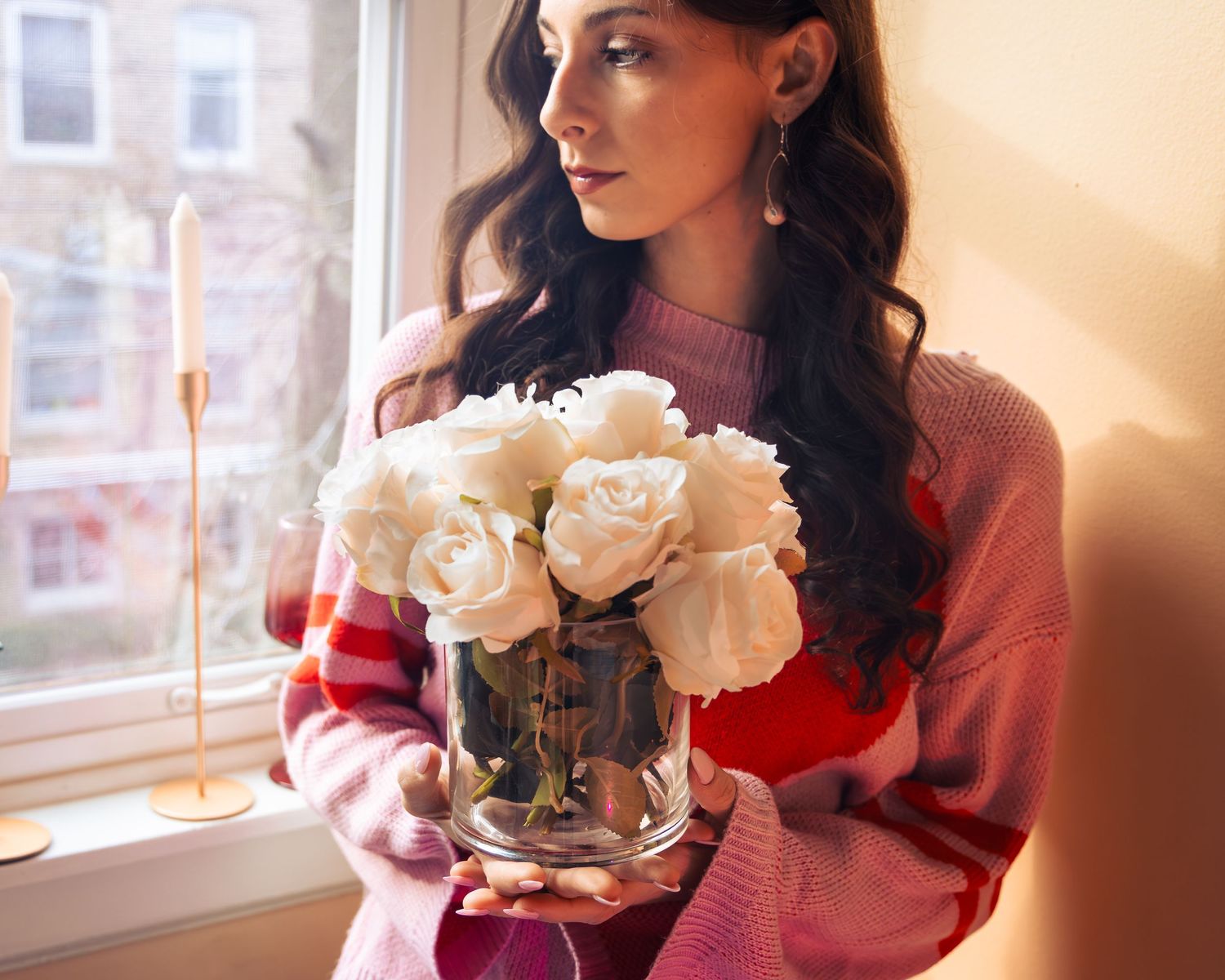 White roses displayed in glass vases near a bright window.