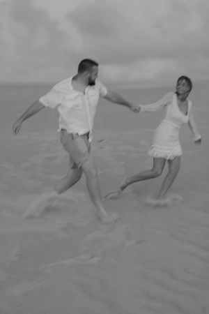 Black and white images of couple playing and running on sandy beach.