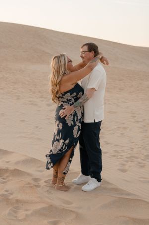 A couple dances intimately together on sandy desert dunes during a romantic photoshoot at sunset.