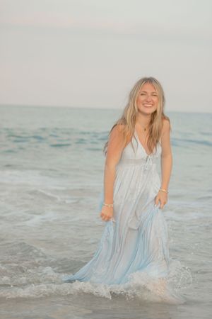 A playful sequence of a woman splashing in ocean waves while wearing a flowing white dress.