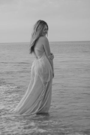 Artistic black and white series of a person wading into the ocean wearing a flowing dress.