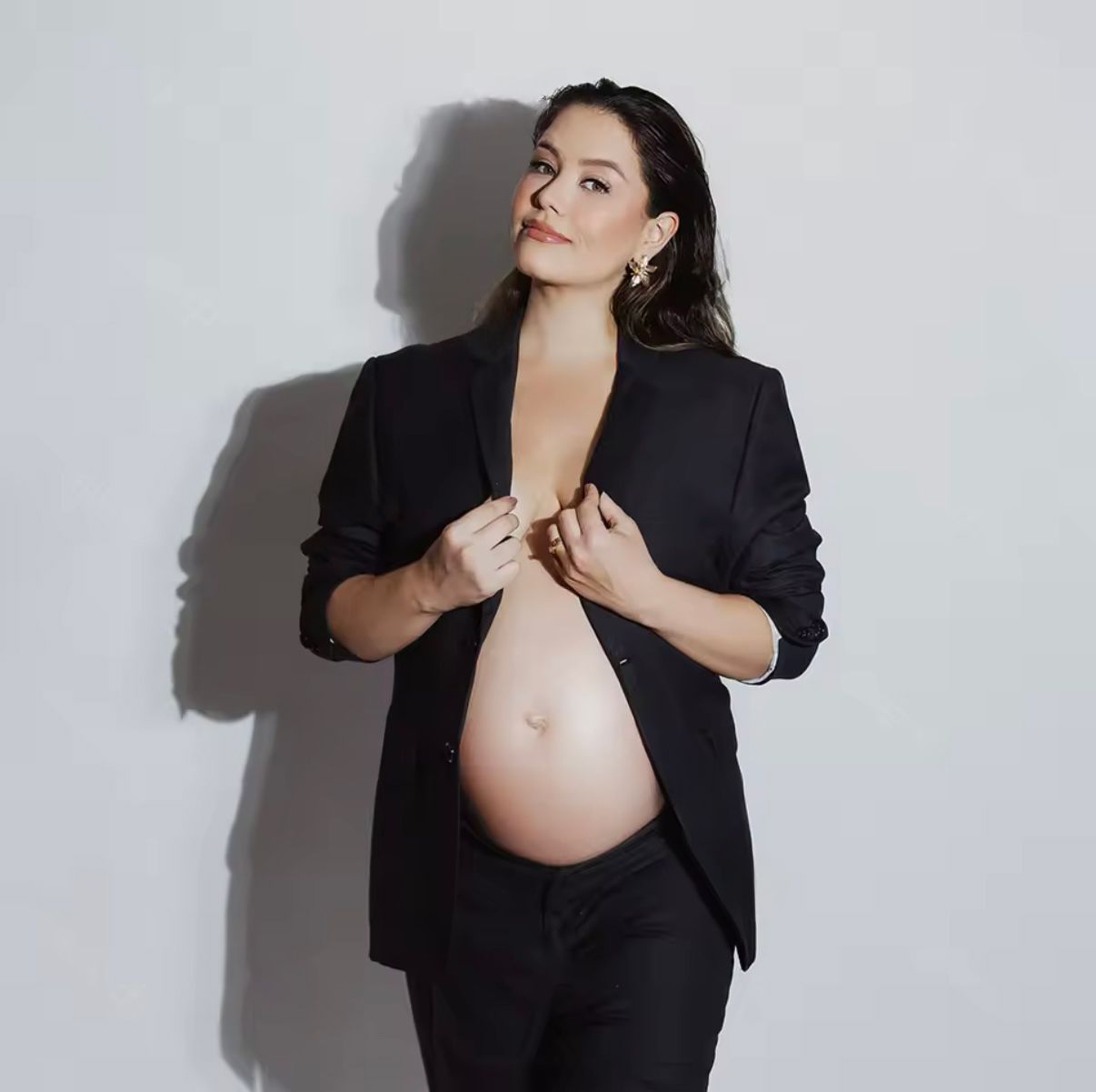 Maternity portrait featuring a pregnant woman in a black blazer against a white background.
