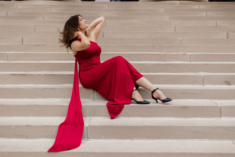 Woman in flowing red dress reclining gracefully on concrete steps.