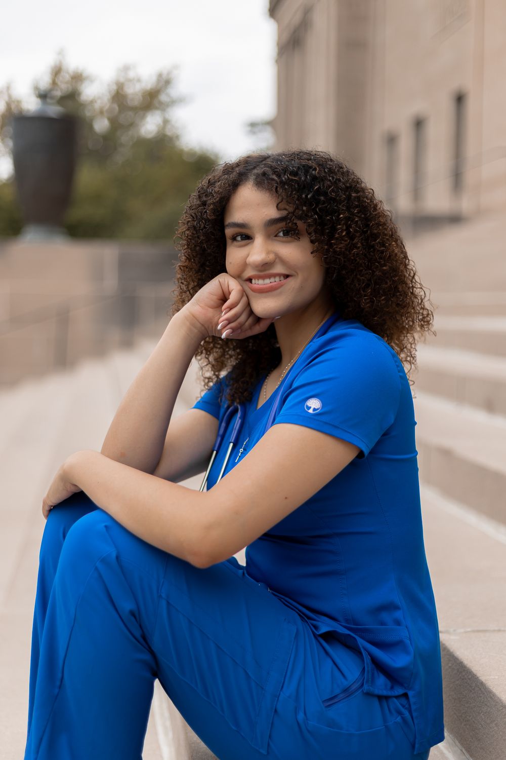 Person in bright blue medical scrubs sitting on concrete steps outdoors.