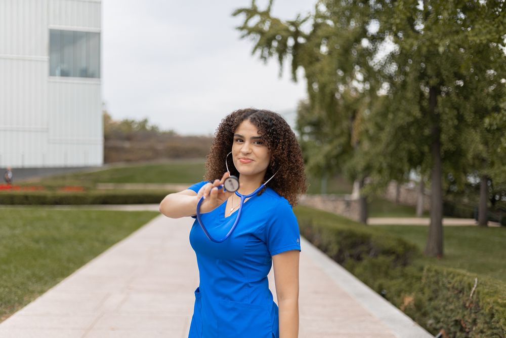 A woman in a bright blue shirt poses outdoors against a scenic rural backdrop.