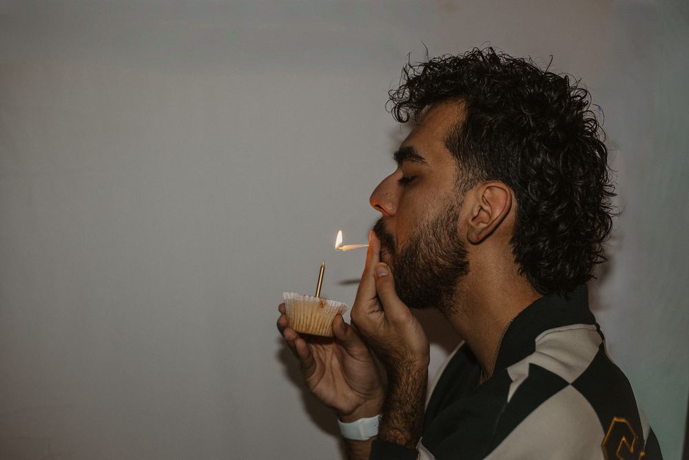 Person in black and white jacket lighting a candle in a dimly lit setting.
