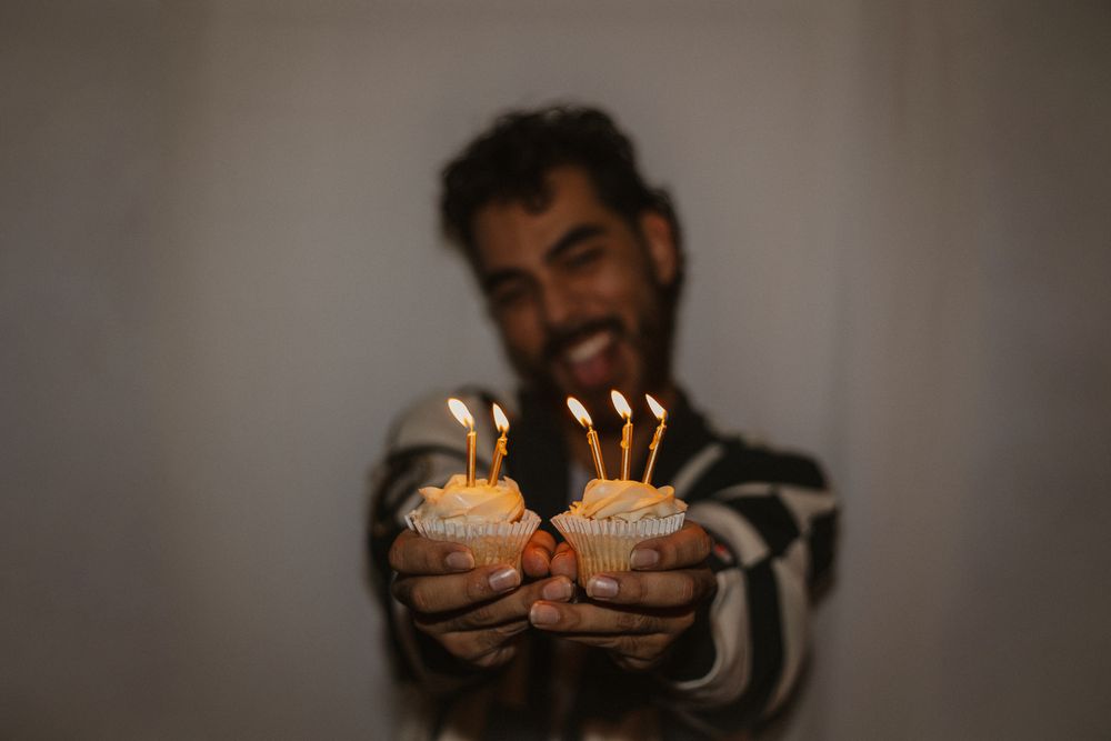 Hands holding lit birthday cupcakes against dark background.