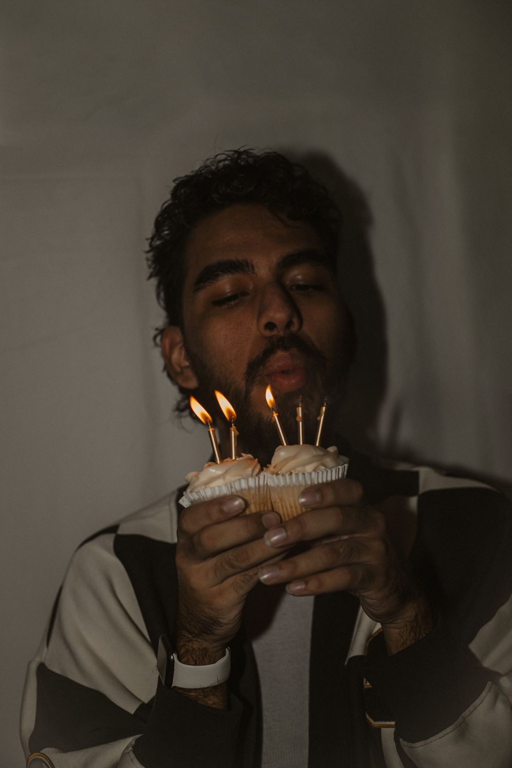 Person blowing out birthday candles on cupcakes in dark moody setting.