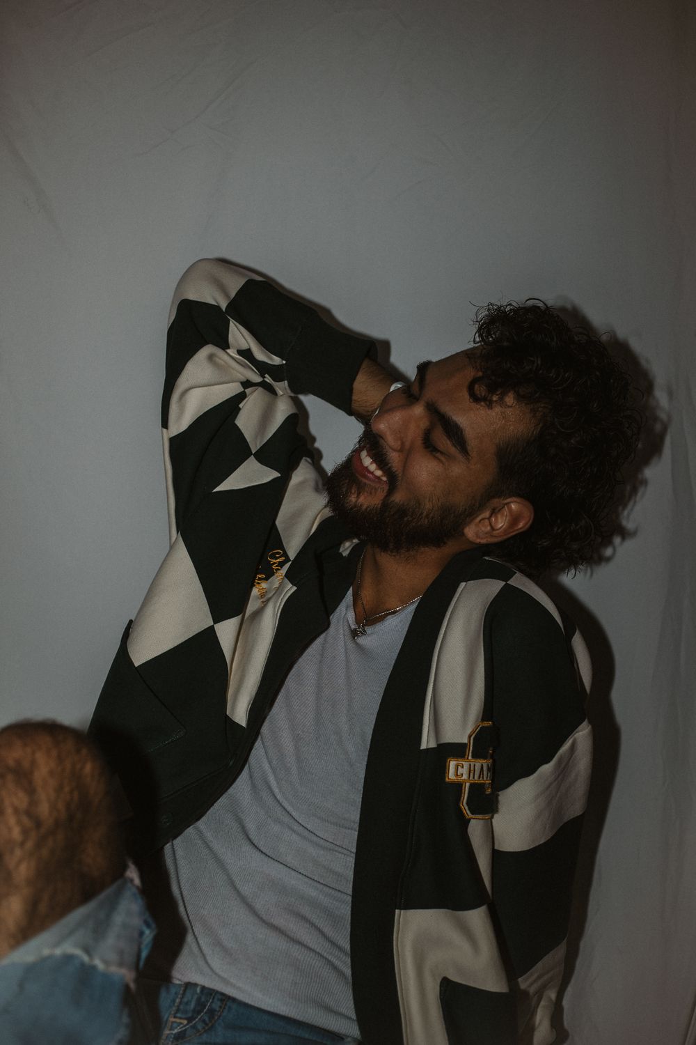 Person in a geometric patterned jacket laughing joyfully against a gray background.