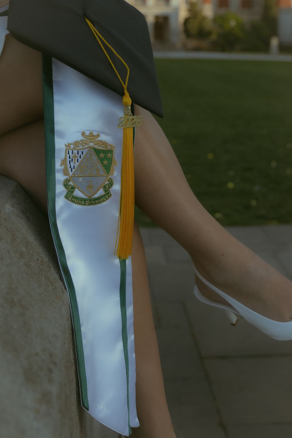 Graduate wearing a white satin stole with gold tassel and embroidered crest on graduation cap.