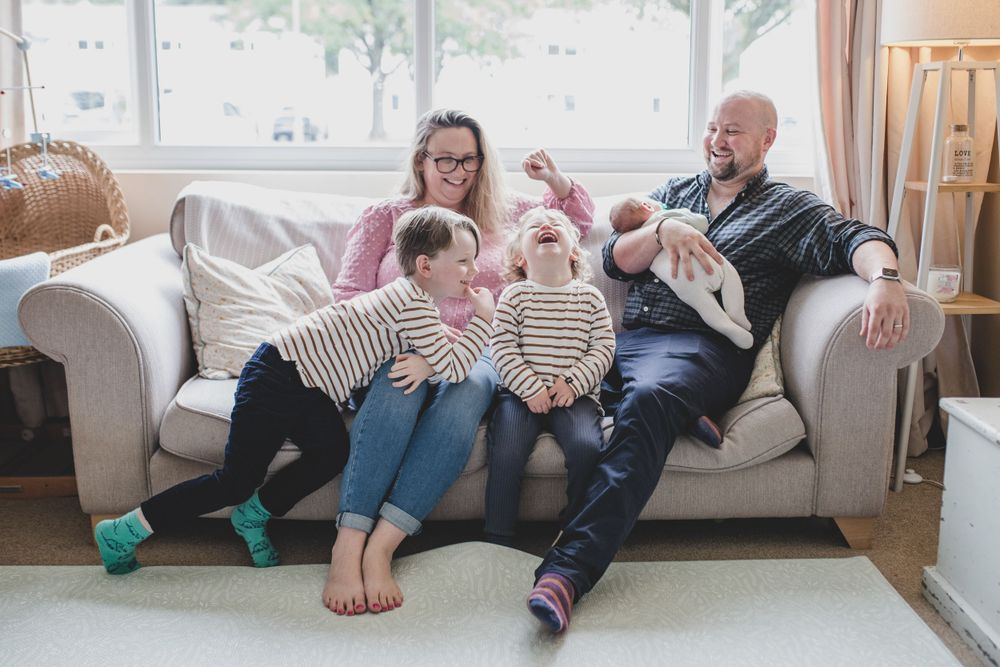 A family shares joyful moments together while relaxing and laughing on a cozy white couch in their living room.