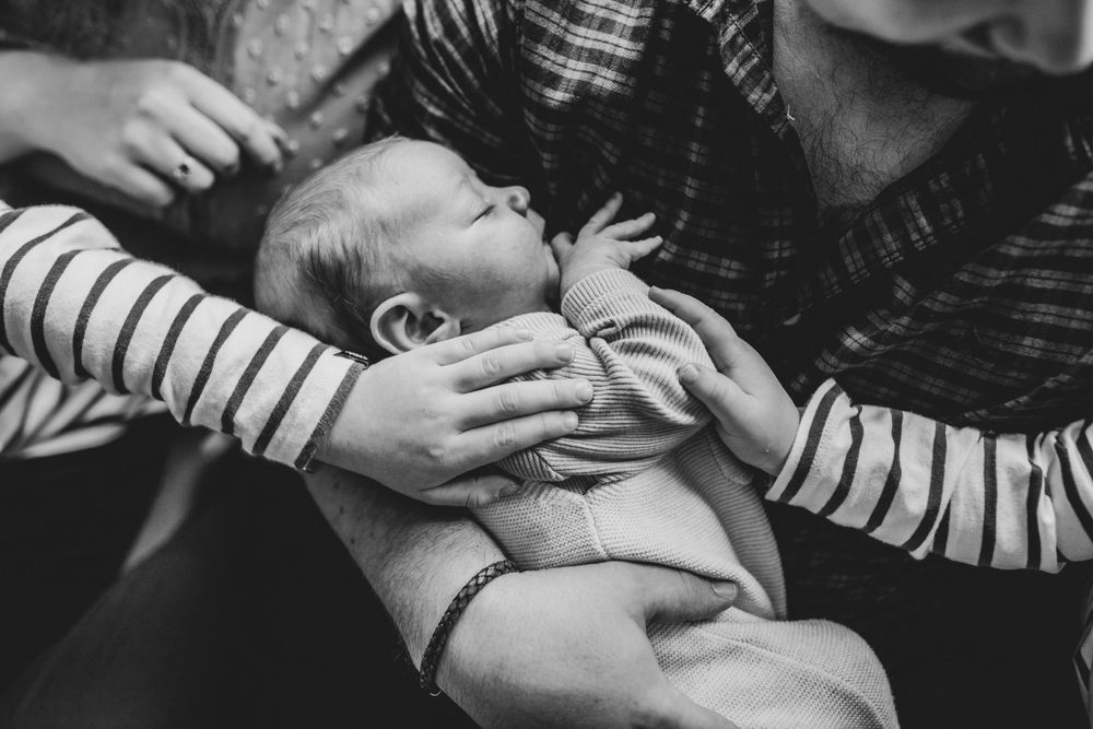 An infant is cradled in gentle hands wearing striped sleeves during an intimate black and white moment.