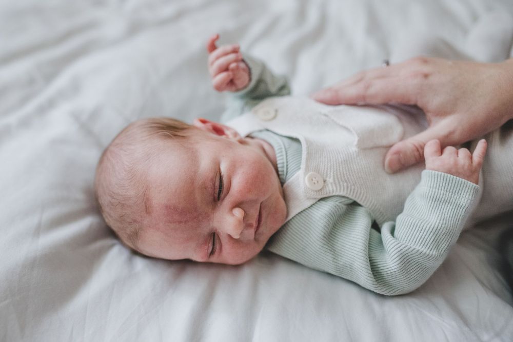Peaceful sleeping newborn baby wearing soft mint colored onesie lies on white bedding.