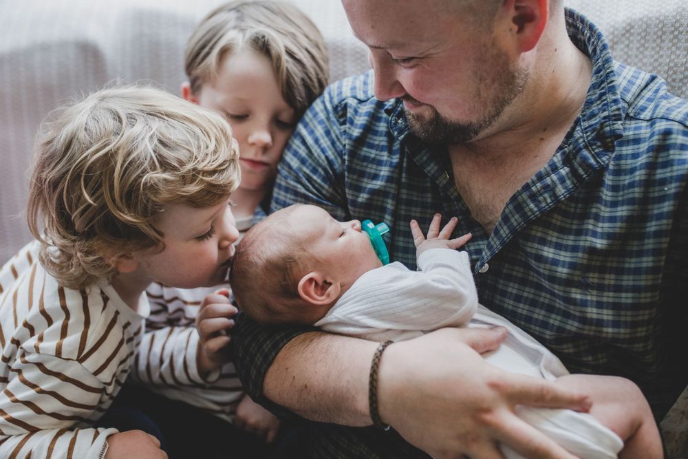Family shares tender moment with their newborn baby while sitting close together on couch.