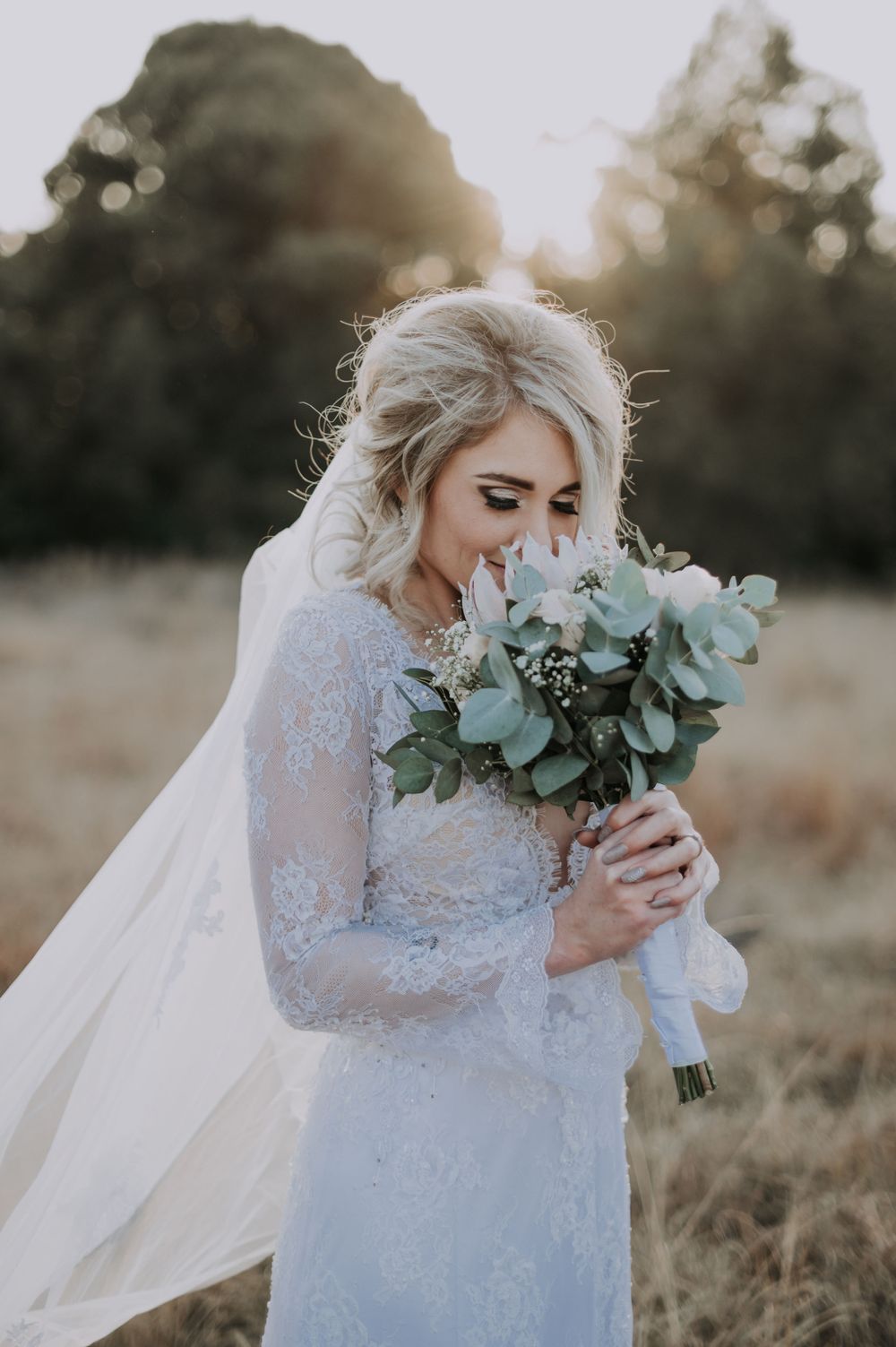 Bride in lace wedding dress holding a eucalyptus bouquet during sunset.