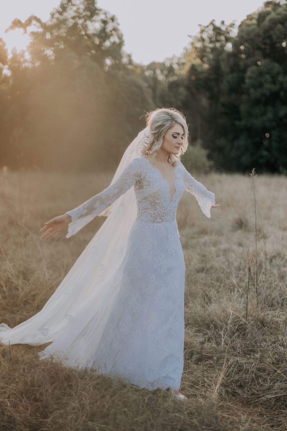 Bride in flowing lace dress twirling in a sunlit field with flowing veil.